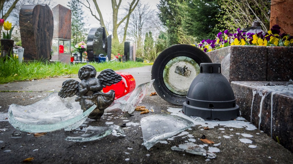 Ein zerstörtes Grablicht und ausgelaufenes Kerzenwachs liegen auf dem Weg eines Friedhofs