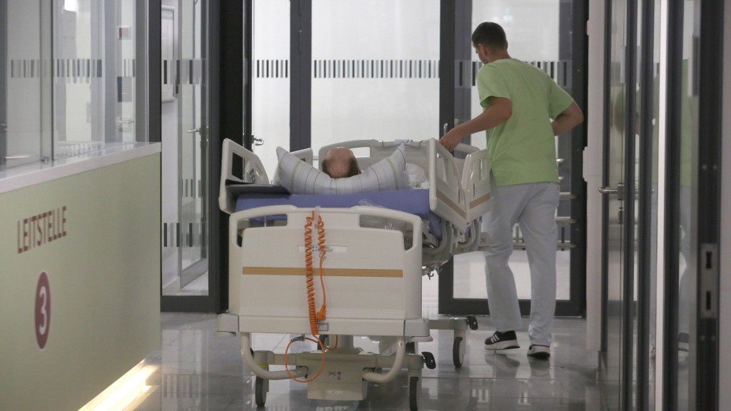 Ein Patient wird im Krankenbett von einem Pfleger über den Flur geschoben.