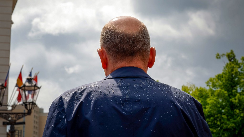 Olaf Scholz mit dem Rücken zur Kamera mit nassem Regenmantel