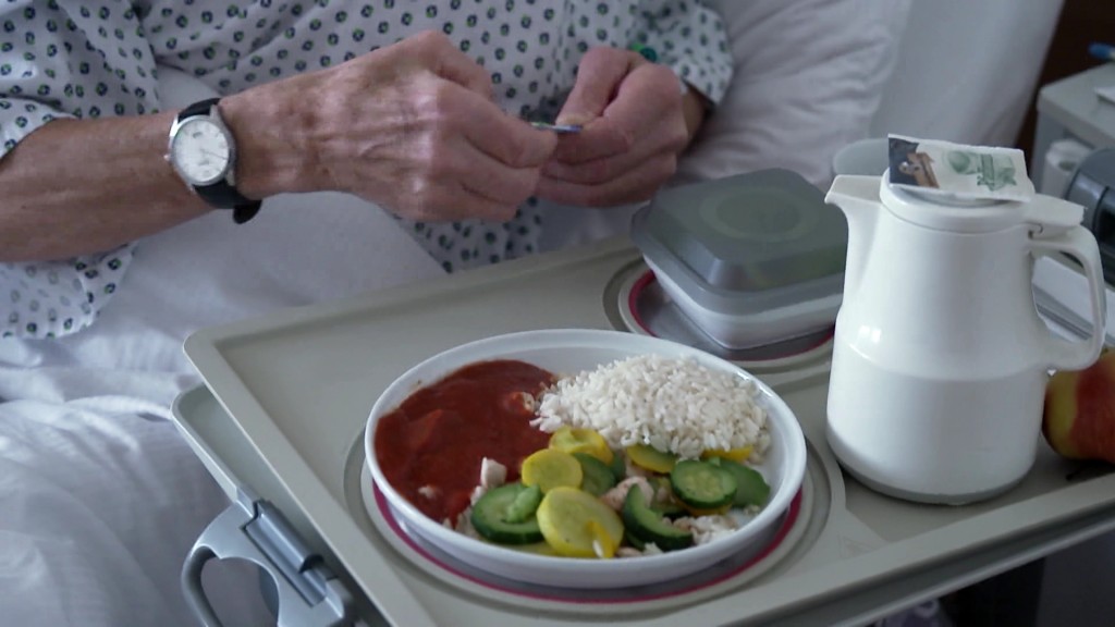 Foto: Eine Person bekommt ihr Essen an einem Krankenhausbett: Der Teller ist gefüllt mit Reis, gelber und grüner Zucchini und Tomatensauce