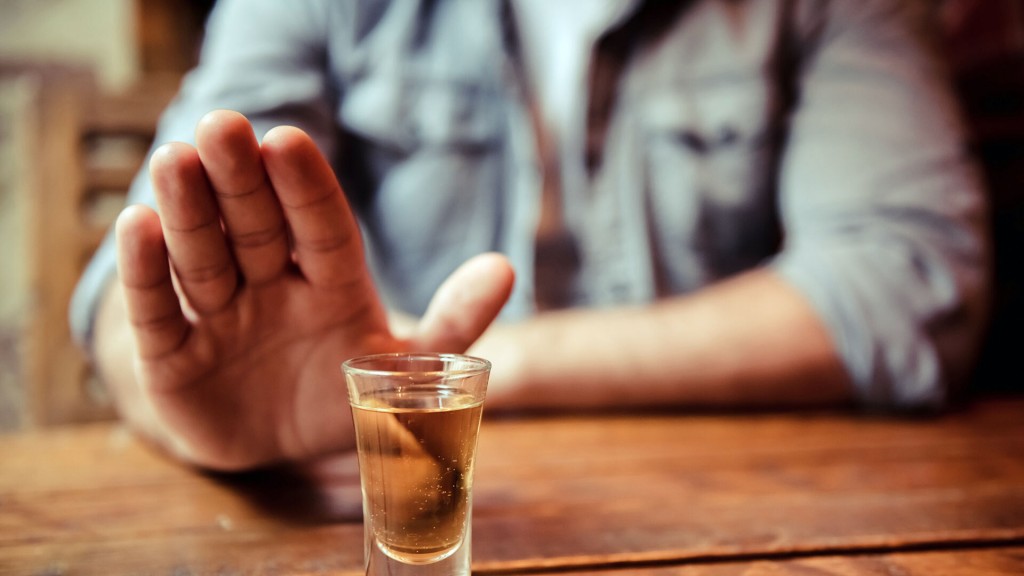 Ein Mann sitzt am Tisch und hält seine Hand ablehnend vor ein alkoholisches Gestränk