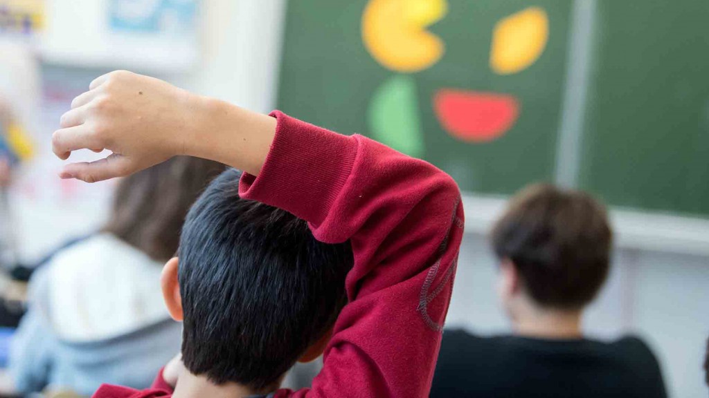 Foto: Ein Junge sitzt mit dem Arm überm Kopf in einer Grundschulklasse