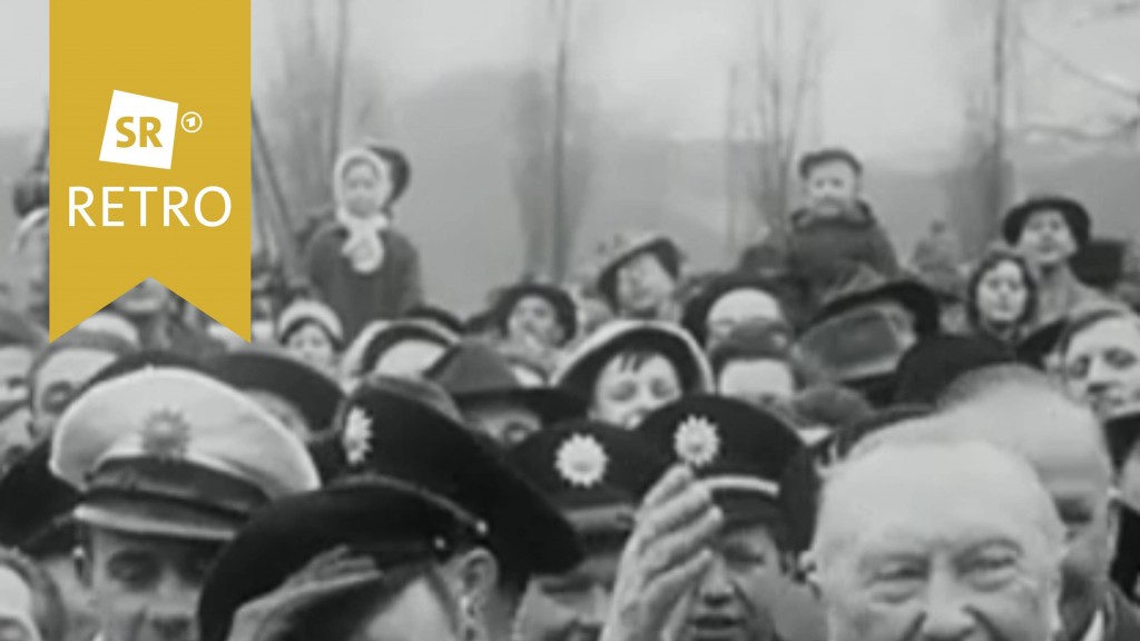 Konrad Adenauer bei seinem Empfang im Saarland im Januar 1957. Er winkt. Um ihn herum viele Polizisten und Bürger