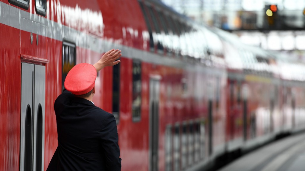 Ein Zugbegleiter steht neben einer Regionalbahn am Bahnsteig.
