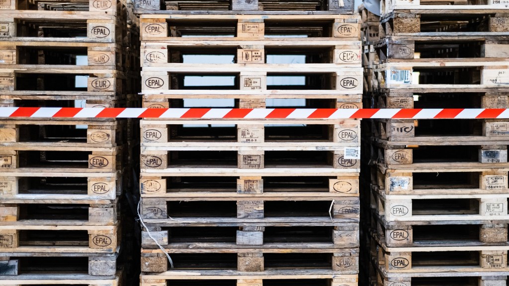 Symbolbild. Zurückgehende Aufträge. Mehrere Stapel Euro-Paletten stehen ungenutzt in einem Lager.