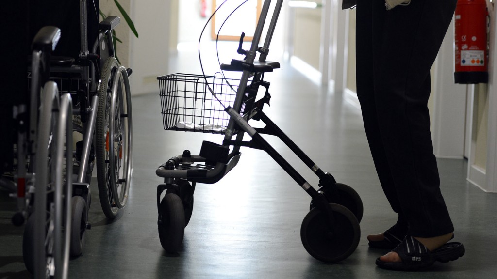 Foto: Eine Bewohnerin eines Altenpflegeheimes steht mit ihrem Rollator im Flur