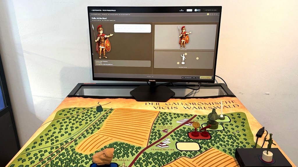 Foto: Interaktive Medieninhalte machen spannende Geschichten zu den vorgestellten Objekten erlebbar. Der Plan des Vicus Wareswald vor dem Bildschirm zeigt, in welchem Bereich die Originalobjekte gefunden wurden.