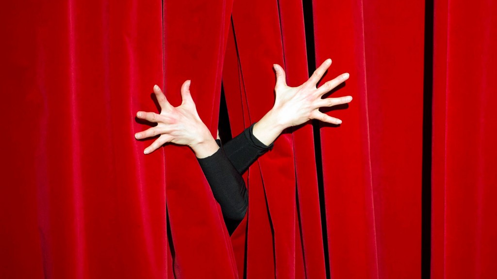 Zwei Hände greifen durch einen Theatervorhang