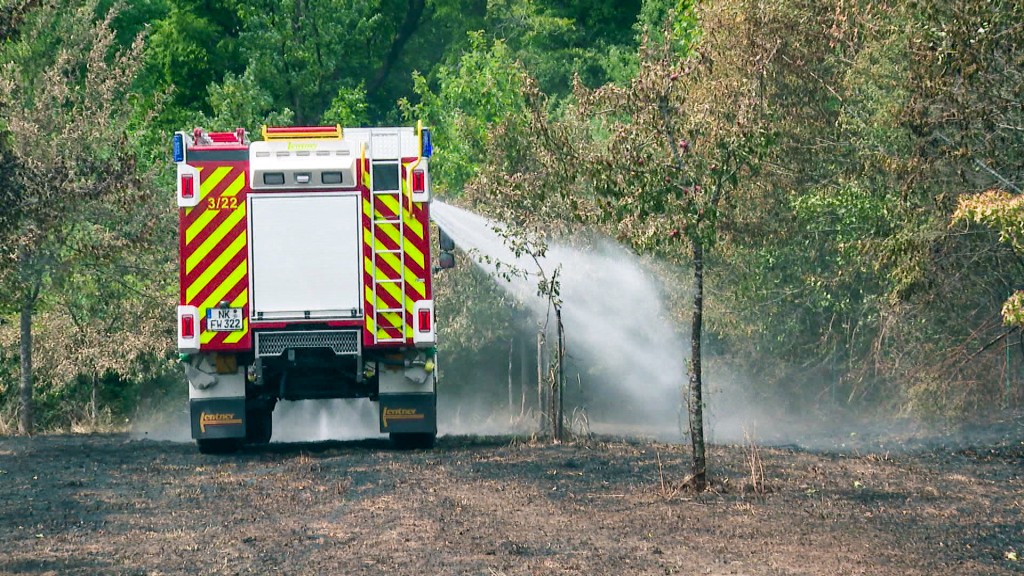 Aus einem Feuerwehr-Einsatzfahrzeug wird Wasser auf eine verbrannt Wiesenfläche bei Wiebelskirchen gesprüht