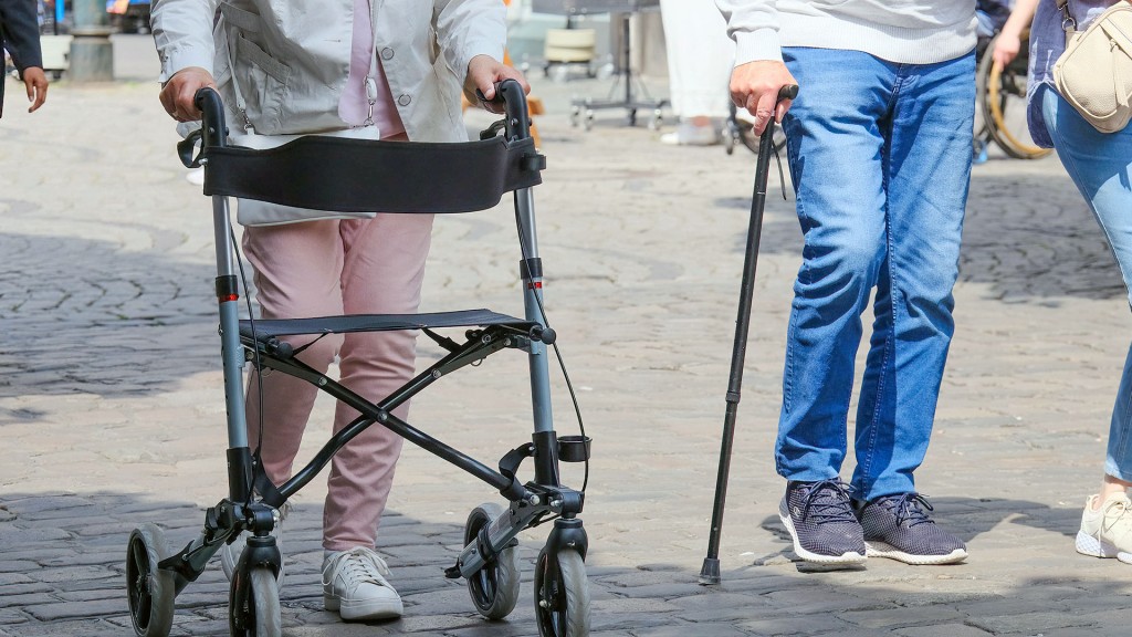 Zwei Senioren mit Rollator und Gehstock in einer Fußgängerzone